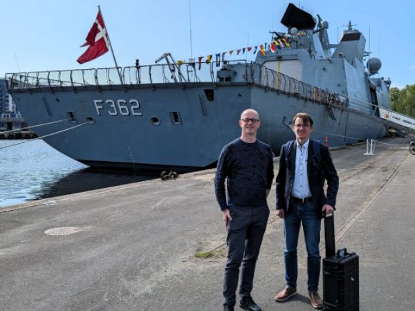 Atrolight Denmark-direktør Peter S. Hansen (t.v.) og moderselskabets direktør  Laurynas Mačiulis, (t.h.), ses her med HDMS Peter Willemoes (F362) i baggrunden.